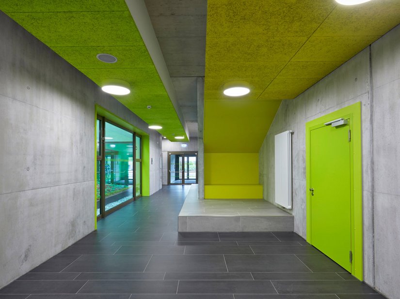 Exposed concrete surfaces and colorful accents in shades of green and yellow create an atmosphere that is transparent yet vibrant on the inside.