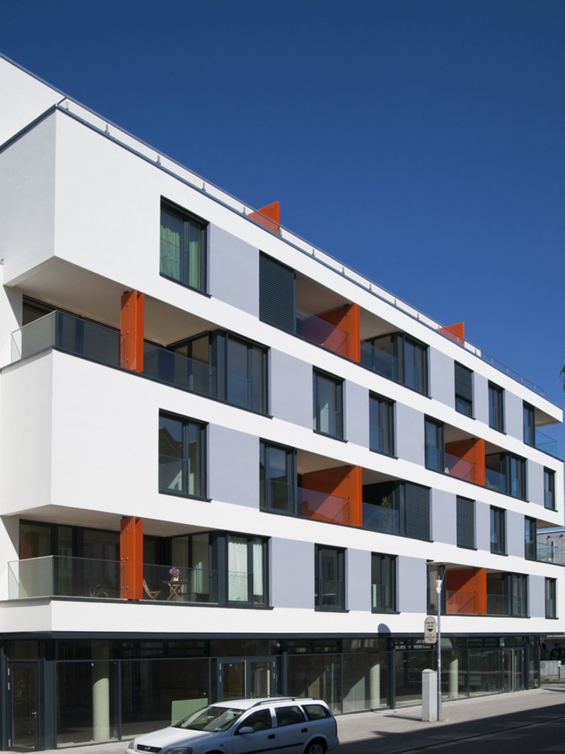 The thermally insulated facade plays with its window openings and the niches of the balconies that dictate the effect of the facade. The orange red sets accents without destroying the impact of the white meander.