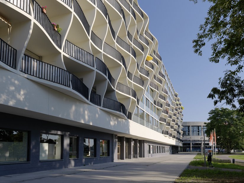 The facade forms an interplay between fully glazed balconies and curved balconies with steel railings.