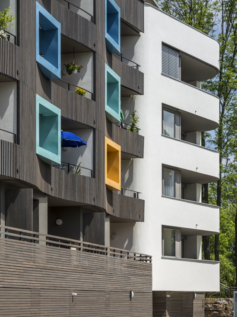 The color shades of the peep-boxes are distributed randomly and create an "artistic" colorfulness against the natural character of the storey-high wooden slats.