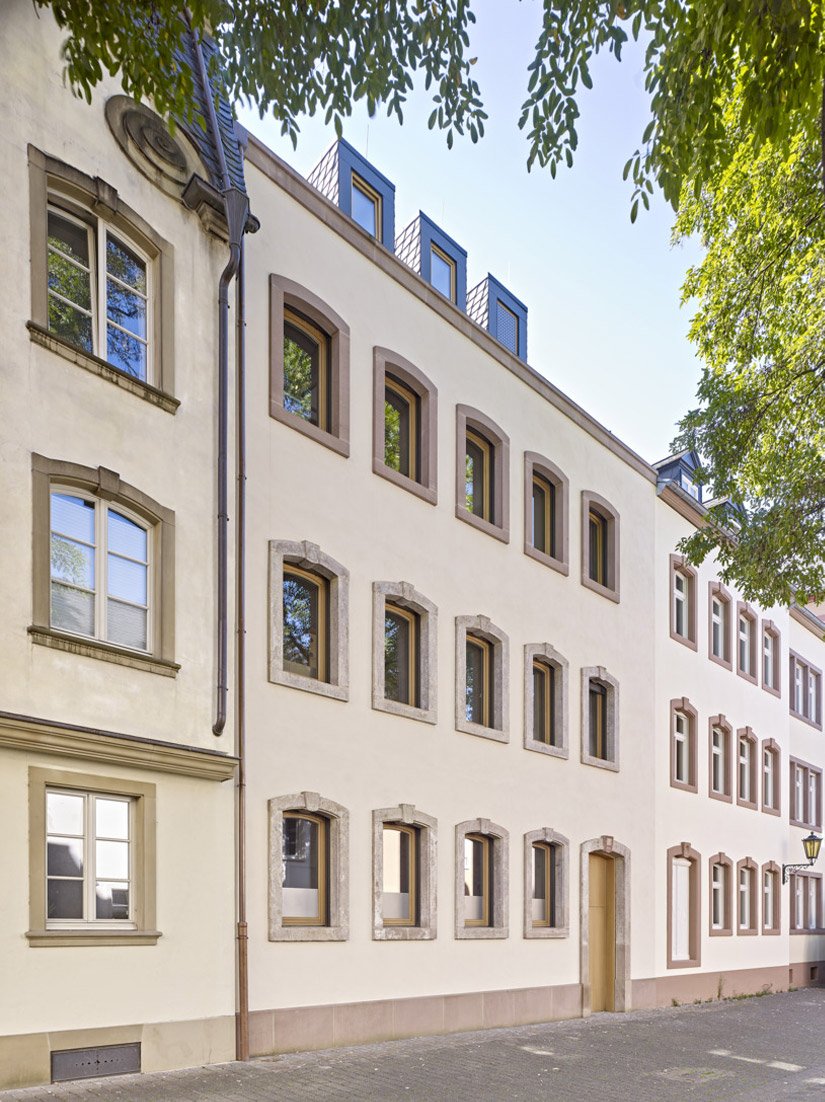 The sandstone window frames of the former existing building were removed before demolition and integrated into the new facade in a new design.