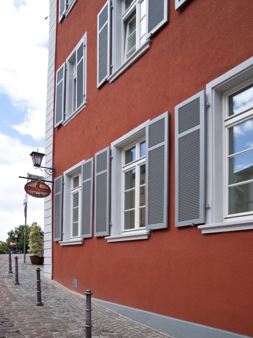 Gray shutters and white windows structure the red facade.