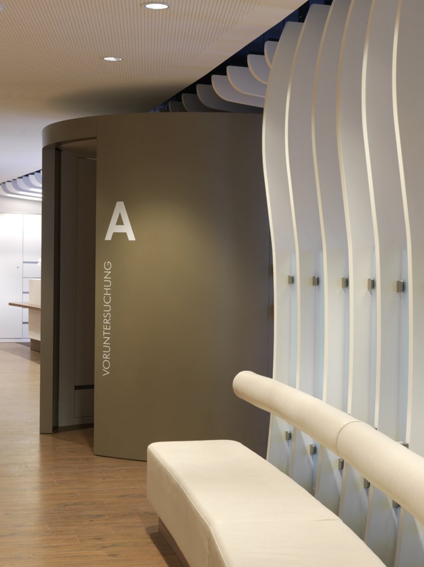 Wooden slats separate the waiting area in front of treatment island A from the corridor. They adopt the character of the baffle ceiling.