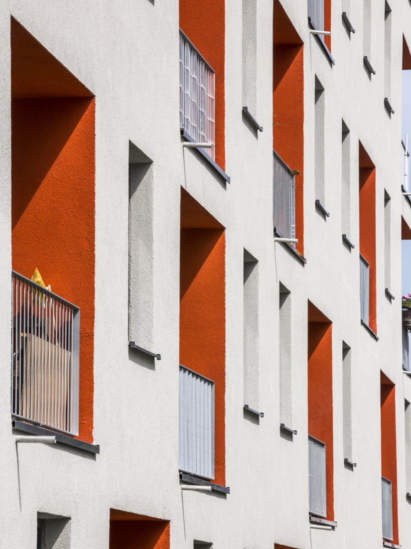 The light gray facade is interrupted by distinctive orange-red balconies.