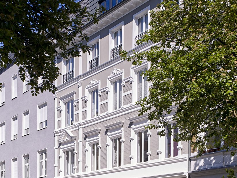 The stylish facade shines in a warm shade of taupe gray. The strongly structured and ornate window frames have been painted white.