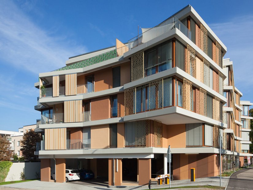 Folds and deliberately decorative elements in warm orange and brown tones lend rhythm to the facade, rendering it welcoming.